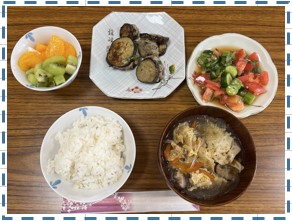 白米とスープとトマトときゅうりの和え物となす料理とフルーツが並べられている写真
