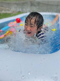 水遊び用のおもちゃがいくつか入っているプールの中で水しぶきをあげながら笑っている子どもの写真
