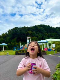 広場で女の子が紫色の飲料水の缶を両手に持って、口を大きく空けながら上を見ている写真