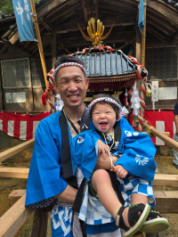 青い法被と鉢巻をした子どもを、青い法被と鉢巻をした大人が片手で抱えているj写真