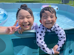 二人の子どもが家庭用プールに入ってにっこりピースをしている写真