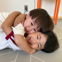 二人の子どもが石でできた床の上に寝そべりながらお互いに抱きしめ合っている写真