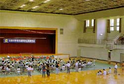 体育館内に敷かれたシートに子供たちが座っている写真