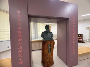 文字が刻まれた台座の上に人物の胸像が置かれ、両側を文字が書かれた門型の枠に囲まれている写真