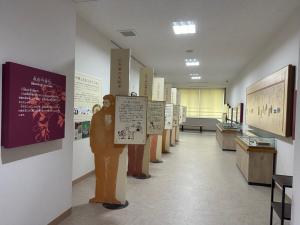 展示室の通路に、人の形を模したパネルに解説文が書かれた立て看板が並び、壁面にも説明パネルや資料が配置されている写真