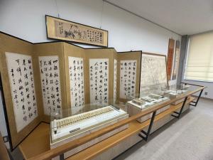 屏風に仕立てられた書作品の前に、ガラスケース入りの資料が並べて展示されている展示室内の写真
