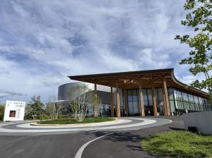 青空の下、木材を使った大きな屋根が特徴的な近代的な建物が建っている写真