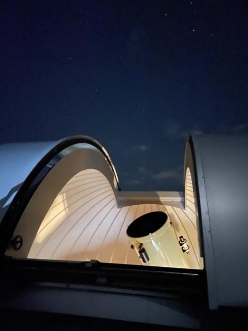 ドーム状の屋根が空き、夜空に向けて設置された天体望遠鏡の写真