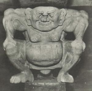 四角い顔で膝に手を置いた中腰の人の石造の写真