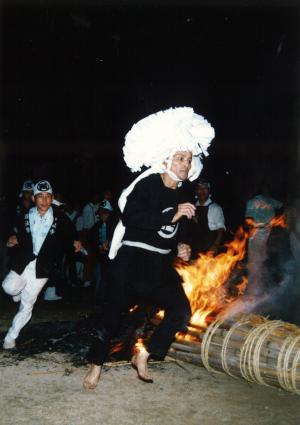 焚火の周りを走る白髪のかつらを付けた男性の写真