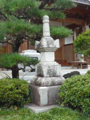 低木や松の木に囲まれた石塔の写真