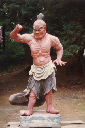 吊り上がった眉毛で上半身裸の男性像が右手を挙げている写真