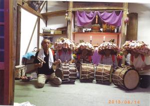 笠をかぶって太鼓をたたく4人と鐘を鳴らす男性の写真