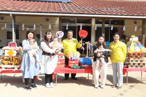 保育園の園庭で子供をだっこしているお母さんたちと団扇を持っているスタッフの写真