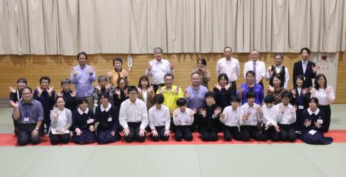 講堂で記念撮影に臨む学生たちと地域の関係者の方々の写真