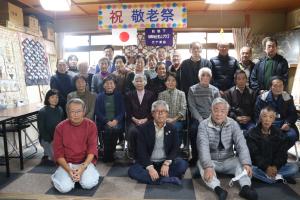 公会堂の部屋で敬老祭の記念撮影に参加している老人クラブの方々の写真