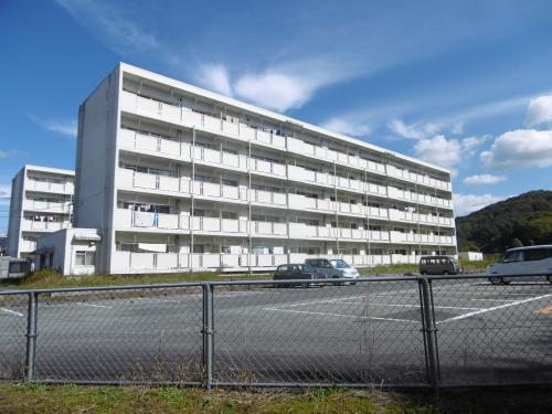 フェンス越しに駐車場と白い5階建の建物が見える町有やなはら住宅の全景写真