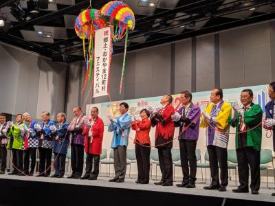 上に吊るされた大きくてカラフルなくす玉の紐を引っ張りくす玉を割る法被姿の人々の写真