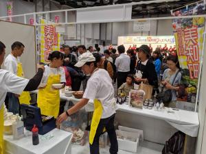 美咲町ののぼりが立つ物販ブースで忙しそうに動く人達と会場を移動するたくさんの人々の写真