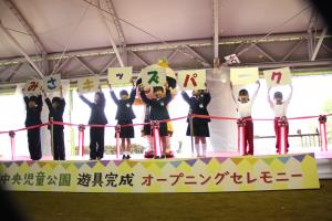 「みさキッズパーク」と1枚に1文字ずつ書かれた紙を頭の上に掲げて立つ児童達の写真