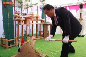 スーツ姿の男性が盛られた土を鍬で崩している写真