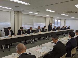 2列に並んだ白い長机に向かい合わせに座り、会議を行うスーツ姿のたくさんの男性達の写真