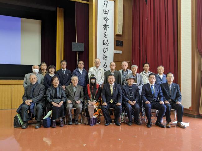 「岸田吟香を偲び語る会」の垂れ幕を背に、前後2列に並んでカメラに向かう男女19名の集合写真
