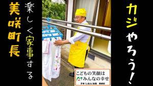 黄色いエプロンと三角巾を身に着けて洗濯物を触っている男性の周りに黒帯で「カジやろう！楽しく家事する美咲町長」と書かれている写真