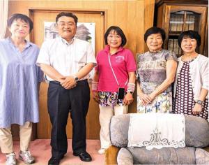 室内で一列に並んで笑顔を見せる女性4人と男性1人の5人組の写真