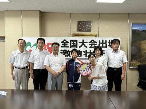 室内でジャージを着用した女性を中心に一列に並ぶ男女の写真