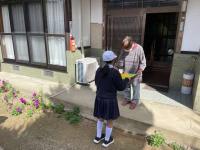 白い帽子をかぶった女子児童が高齢の男性に黄旗を手渡している写真