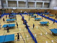体育館内に多くの卓球台が設置され、それぞれで試合が行われている「あさひ・みやすみ卓球大会」の写真