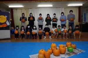 ハロウィンパーティーに参加した大人や子どもたちがカボチャの飾りを持っている集合写真