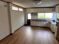 木目調の床が広がる室内に設置された白いシステムキッチンの写真