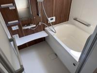 手すり付きの浴槽と鏡とシャワーが配備され、落ち着いた茶色の壁面と白い床が対照的な浴室の写真