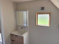 白い壁に木目調の収納がある三面鏡付きの洗面台と四角い窓が設置された洗面所の写真