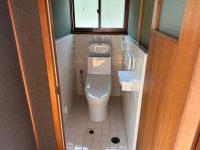 白いタイル張りの壁に囲まれ床にベージュのタイルが敷かれた洋式トイレの写真