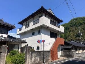 門扉から2階の玄関に向かって赤茶色の階段がある和洋折衷なデザインの白い三階建て家屋の外観写真