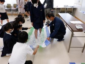 新聞紙で作ったスリッパを履き、ビニールシートの上を歩く女子児童の写真